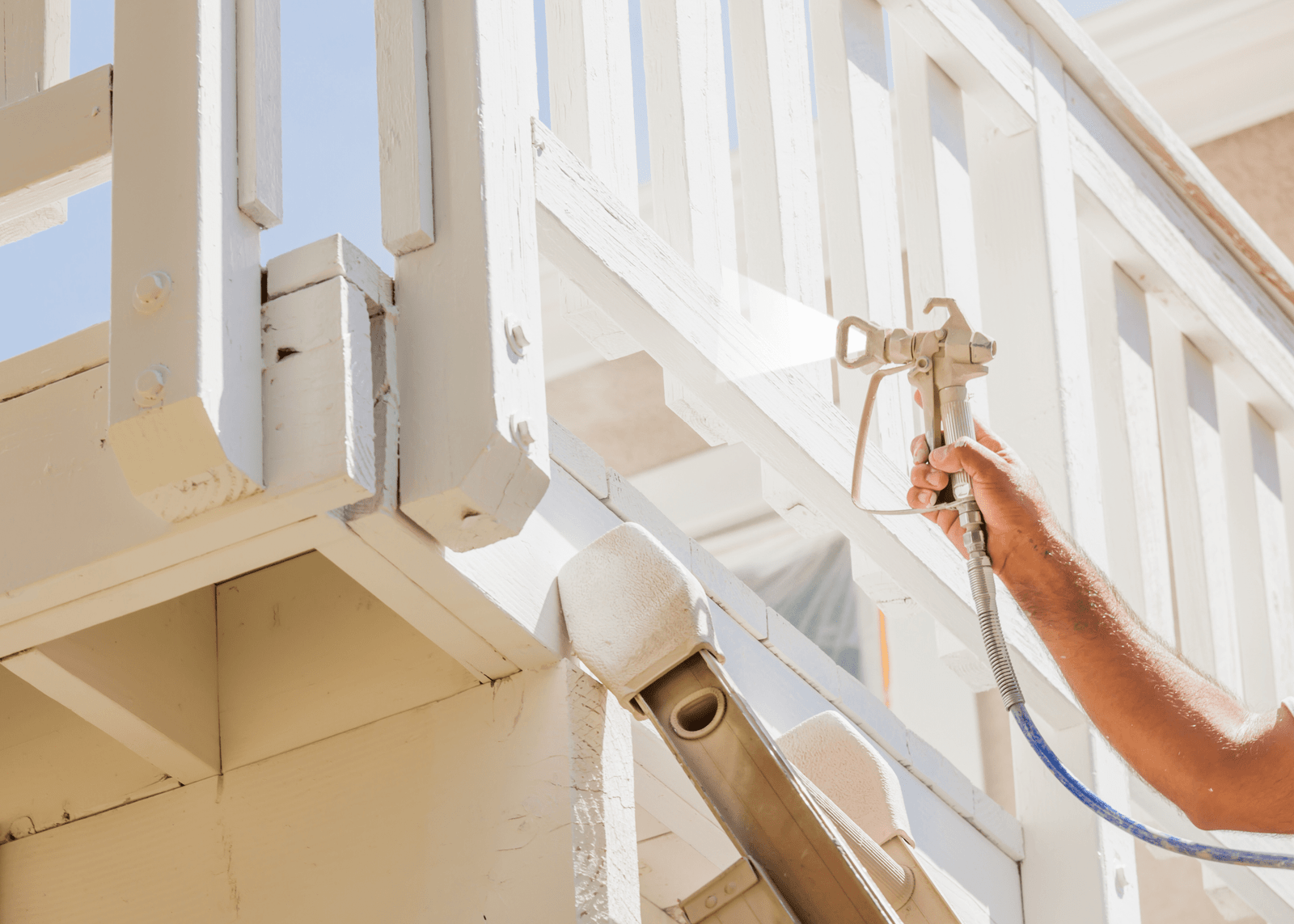 Professional house painter with facial protection spray painting a home deck, offered by Handyman Jax's painting services in Jacksonville, FL.