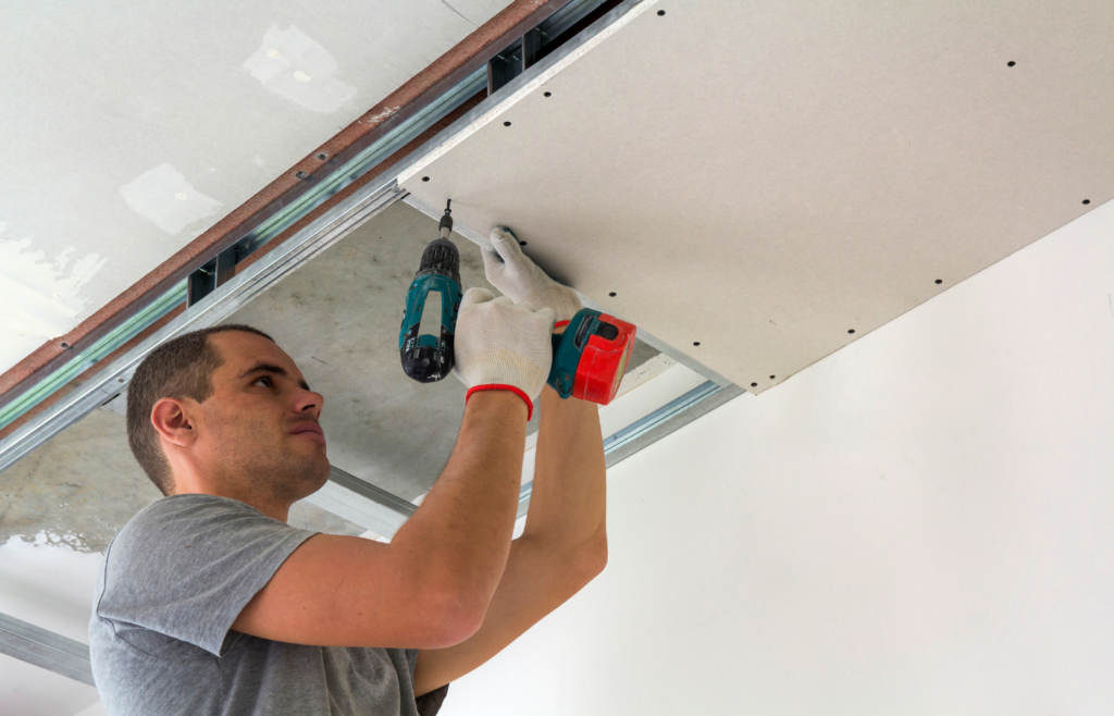 professional at handyman jax fixing a drywall handyman jax professional assemble a suspended ceiling with drywall and fixing the drywall to the ceiling metal frame with screwdriver.